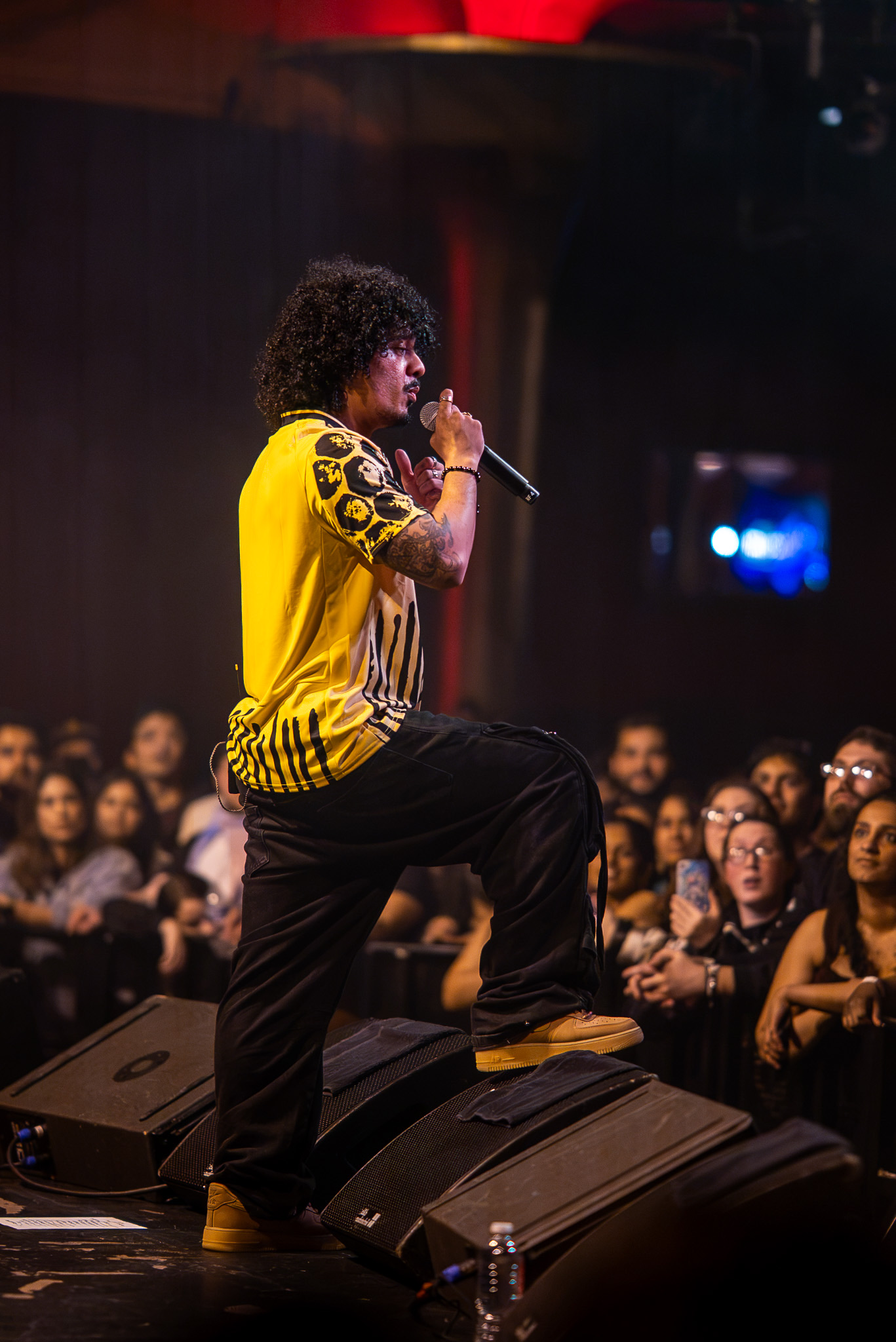 Hanumankind performs at the edge of the stage in a yellow patterned shirt