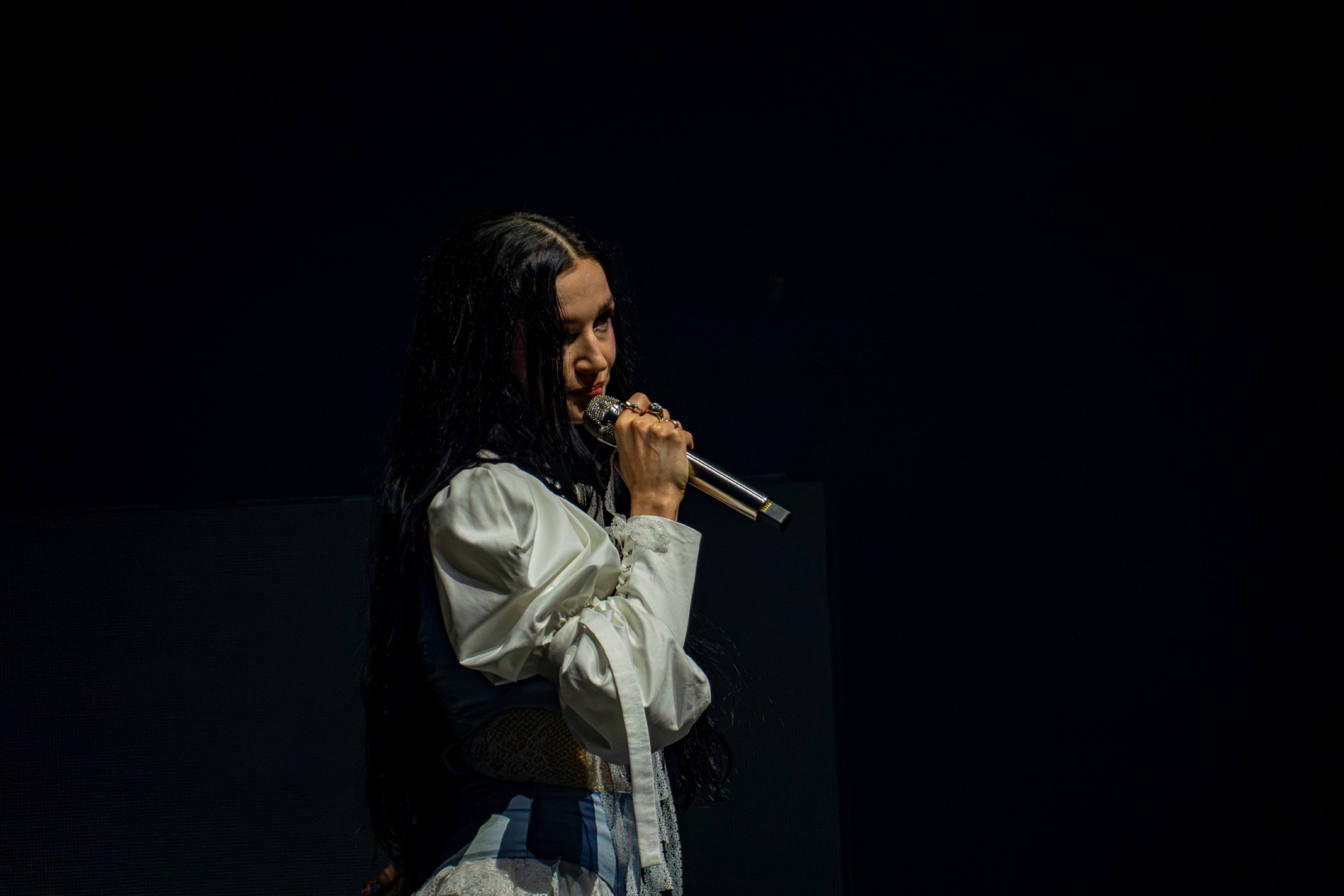 Poppy looks across the room with a handheld microphone at the end of the set