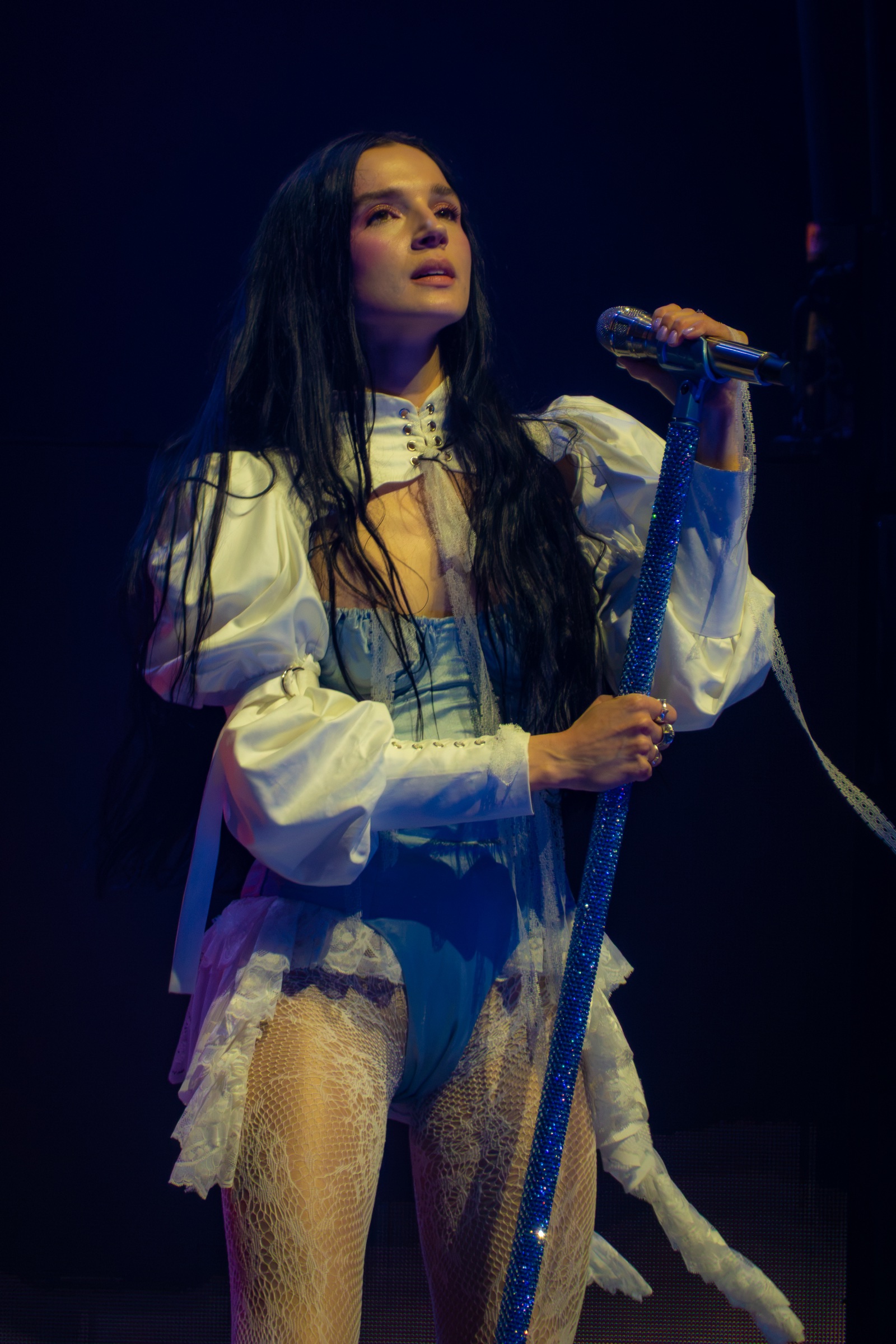 Poppy holds the crystal microphone stand and looks toward the lights