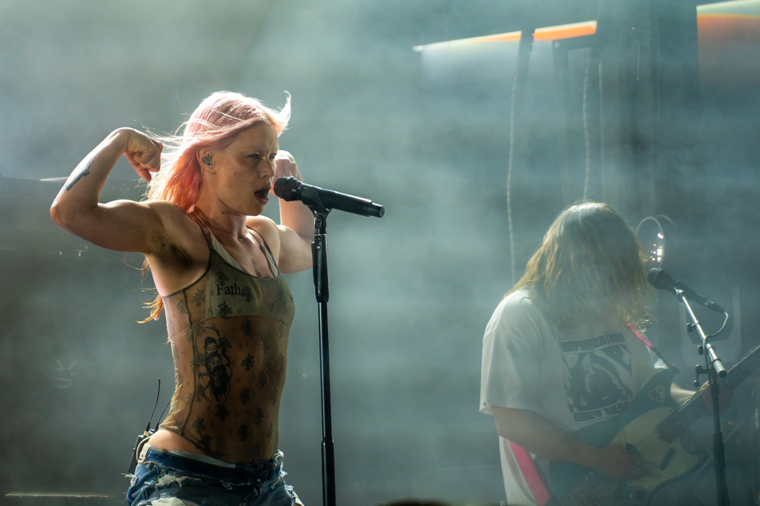 Rhian Teasdale flexing both arms at the microphone as Wet Leg plays behind her