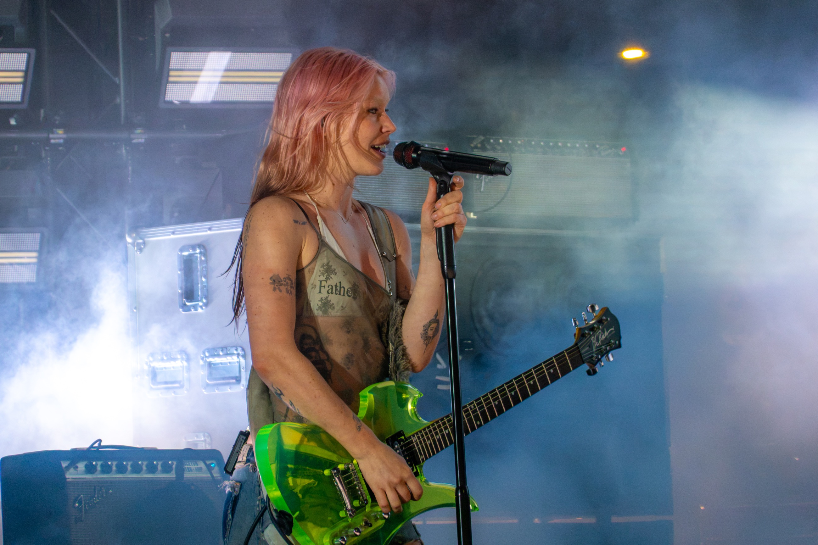 Rhian Teasdale singing with a translucent green guitar beneath blue-white haze