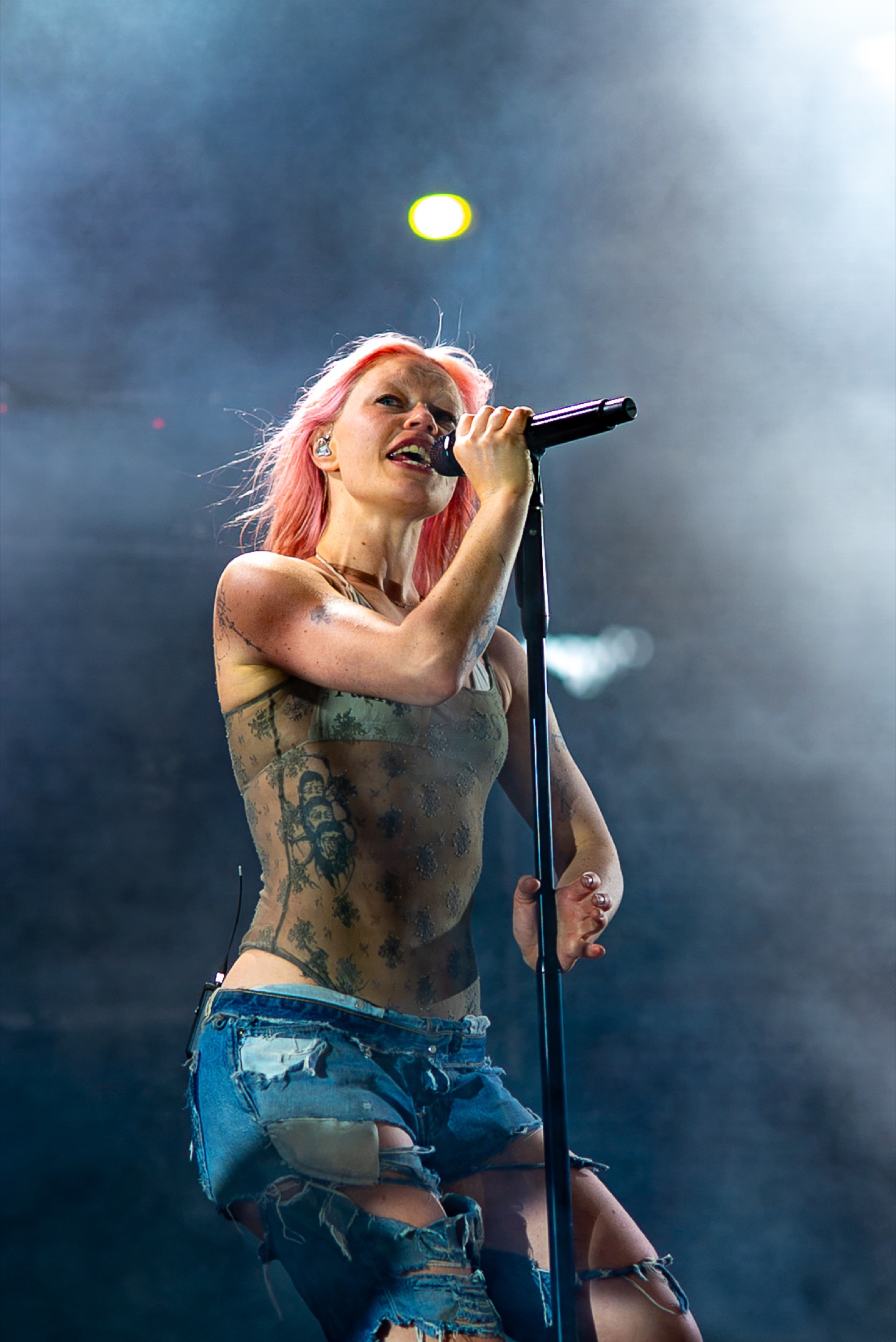 Rhian Teasdale singing into a handheld microphone beneath white stage light